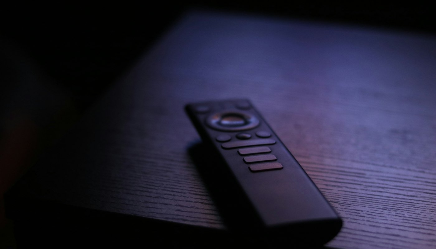 A black streaming remote lying on a dark wooden table in purple light