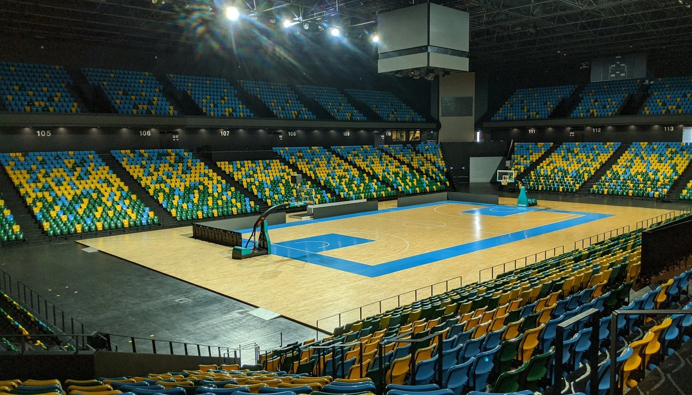 An empty indoor basketball arena with blue and yellow seats around a lit wooden court