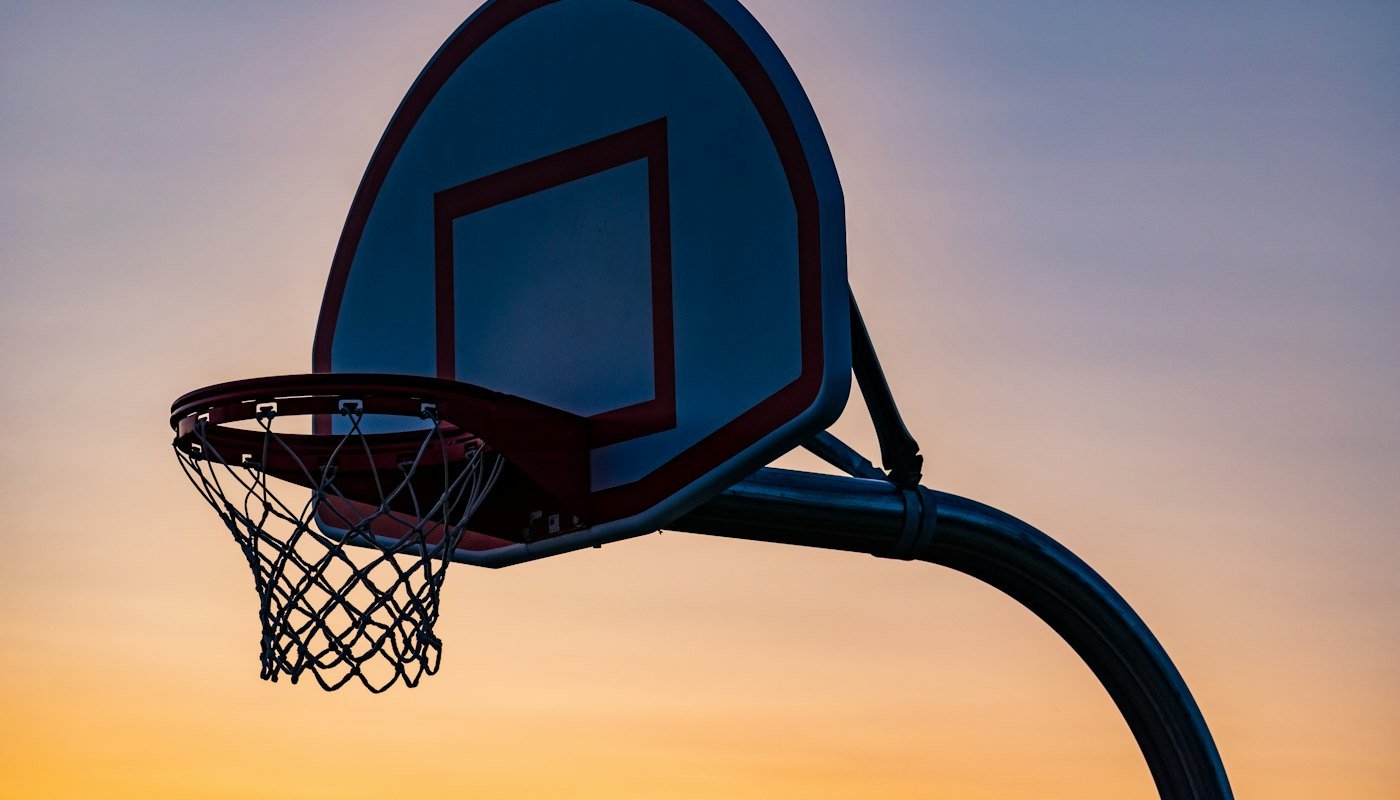 An outdoor basketball hoop and net against an orange and blue sky at sunset